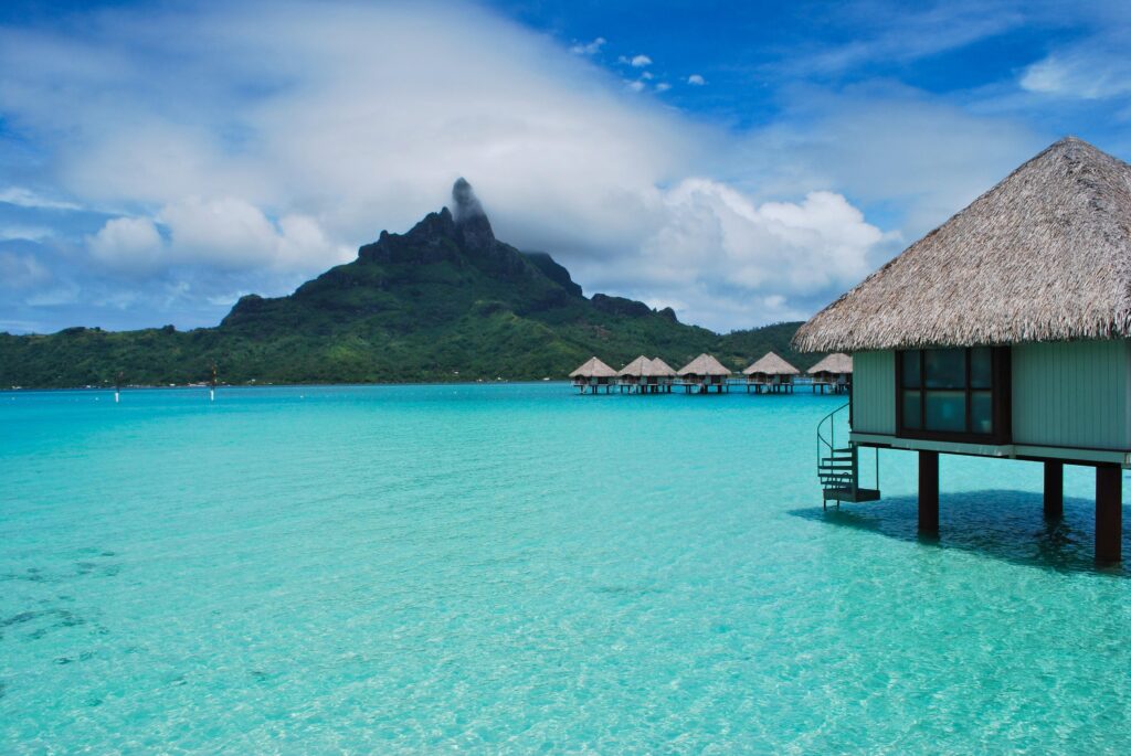 Tropical bungalows above turquoise sea with lush green mountain and dramatic cloudscape wallpaper