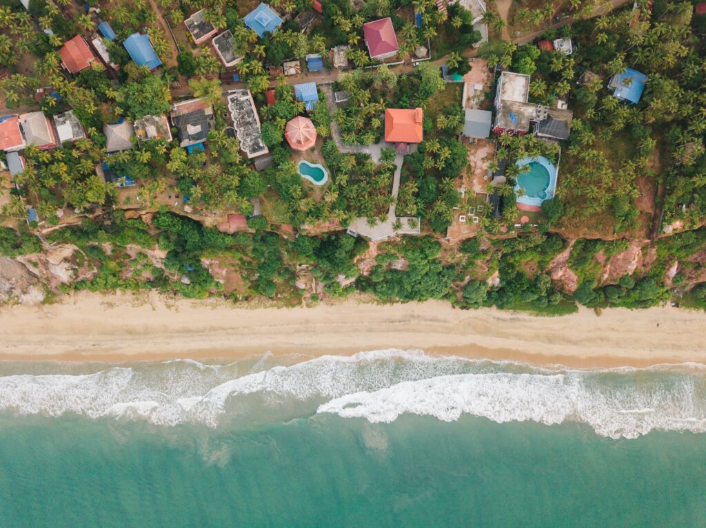 Aerial view of tropical coastline with palm trees colorful buildings pools golden beach and turquoise waves Wallpaper