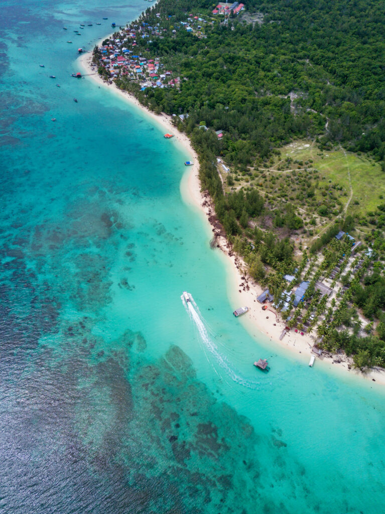 Aerial view of turquoise sea sandy beach lush forest coastal village and boat on clear water Wallpaper