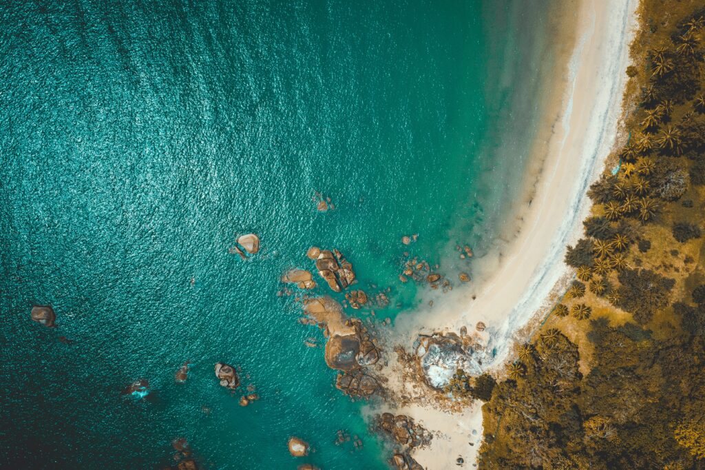 Aerial view of vibrant tropical coastline with turquoise sea sandy beach palm trees and rocks Wallpaper