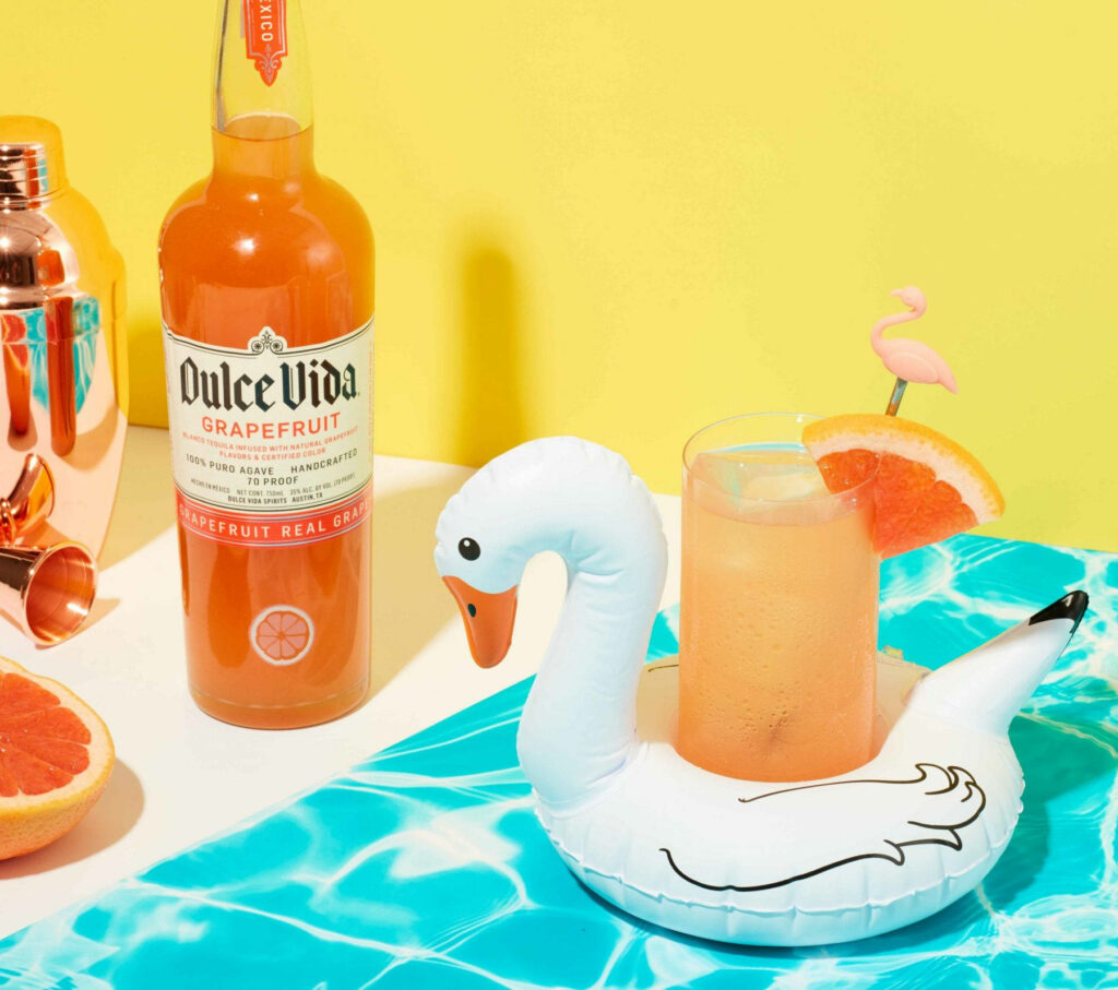Vibrant Dulce Vida grapefruit cocktail on inflatable swan with tropical summer party decor background Wallpaper