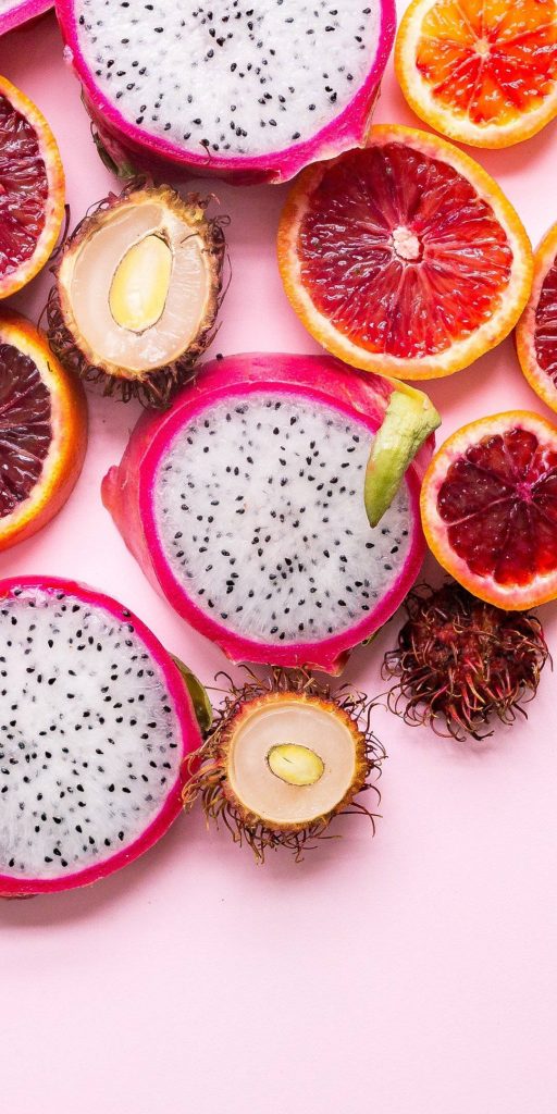 Flat lay of tropical fruits dragon fruit blood orange rambutan on soft pink background wallpaper