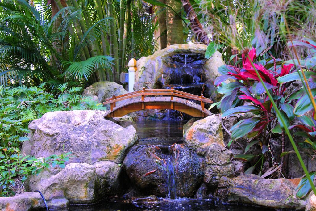 Tranquil interior garden wallpaper with lush palms colorful foliage wooden bridge and waterfall