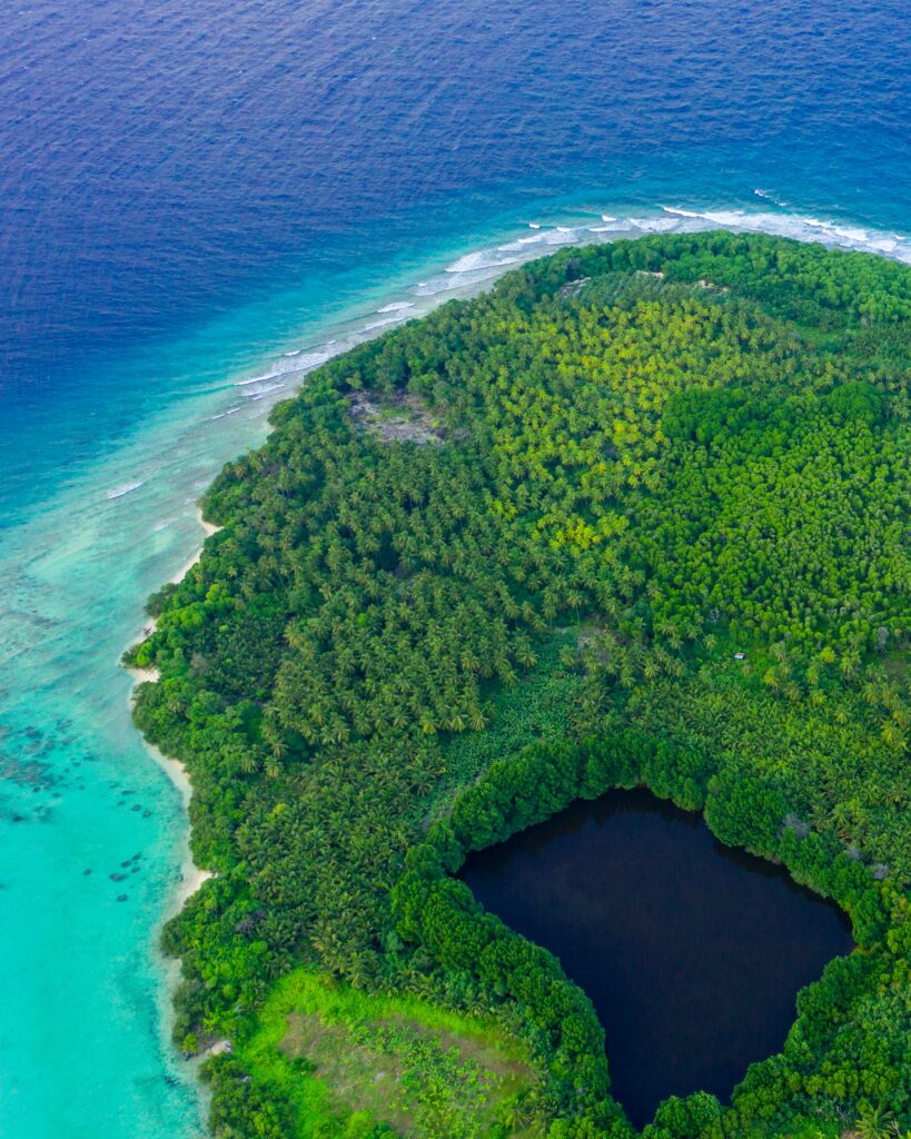 Aerial view of lush tropical island with turquoise lagoon dense greenery and dark central lagoon Wallpaper