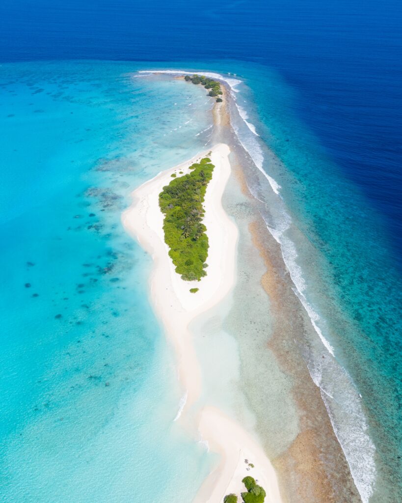 Aerial view of narrow tropical island with lush trees white sandy beaches and turquoise ocean waters Wallpaper