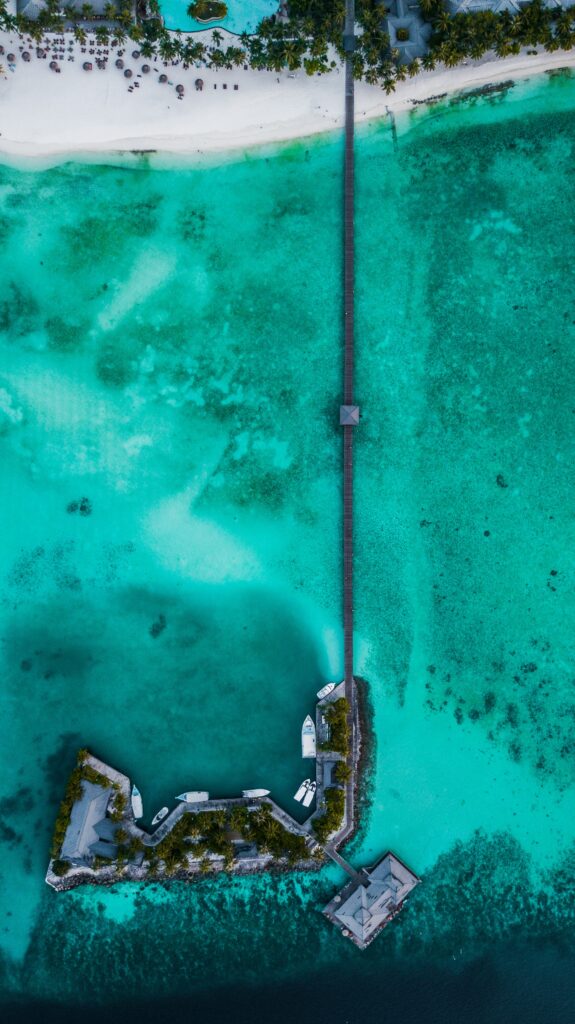 Aerial view of tropical island with long pier over turquoise water and white sandy beach wallpaper