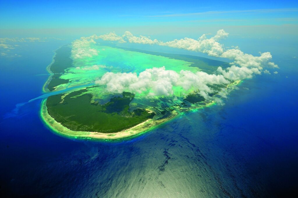 Aerial view of tropical island with lush greenery deep blue ocean and white cloud shadows Wallpaper