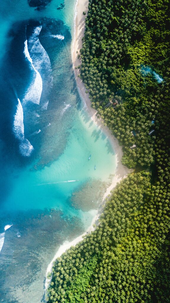 Aerial view of tropical island with turquoise ocean waves and lush green trees coastline wallpaper