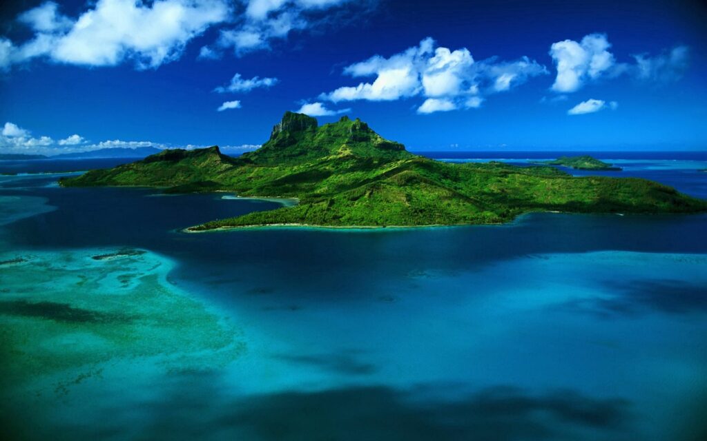 Tropical island with lush greenery surrounded by turquoise ocean under a blue sky with clouds Wallpaper