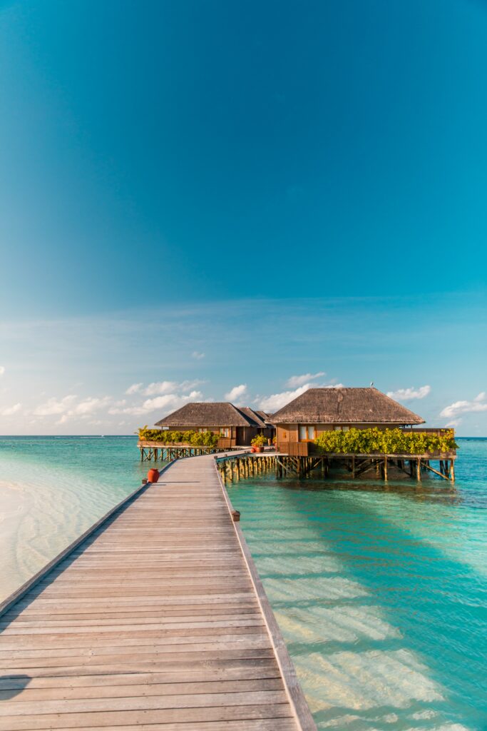 Wooden pier to tropical bungalows over clear turquoise sea under bright blue sky summer island paradise Wallpaper