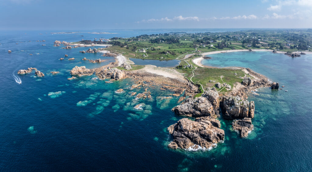 Lush island with vibrant greenery and rugged rocks surrounded by clear turquoise coastal waters wallpaper