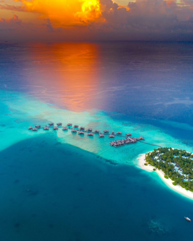 Aerial view of tropical island with turquoise water overwater bungalows and orange sunset beach Wallpaper