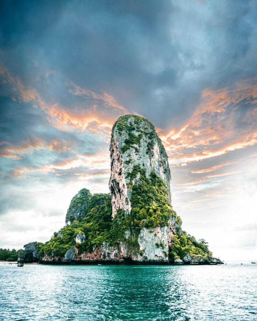 Tropical island with rugged cliffs turquoise ocean and vibrant orange blue sky wallpaper background