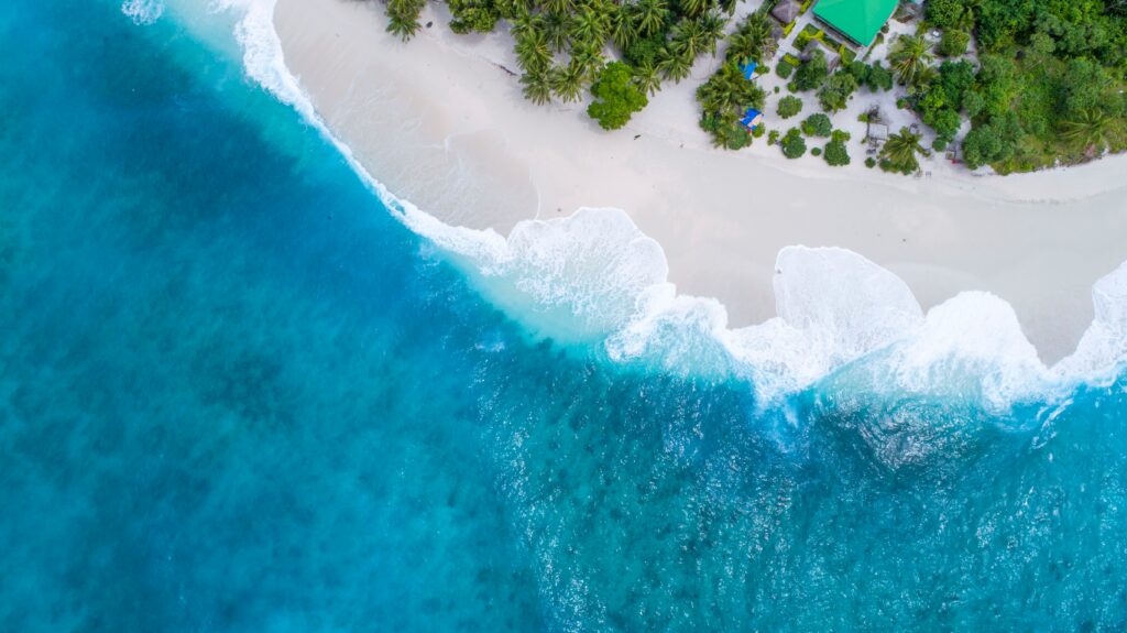 Aerial view of Maldives tropical beach with turquoise waves white sand and lush green palms wallpaper