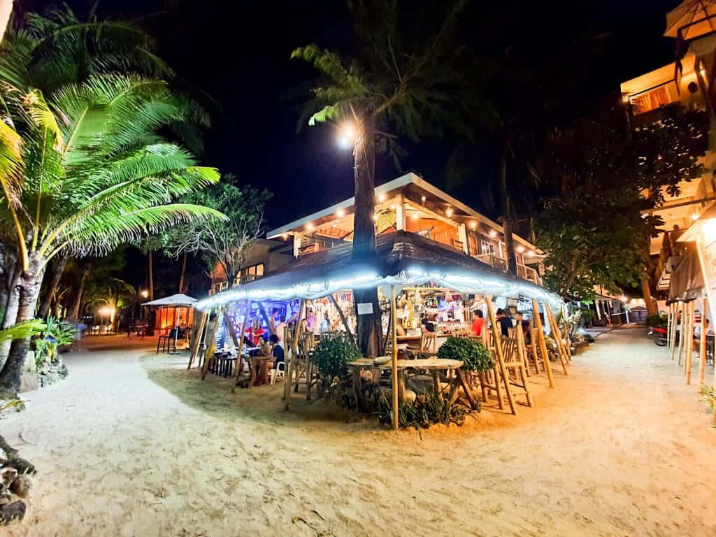 Vibrant Night Beach Scene: Lively Restaurant & Tropical Paradise Wallpaper