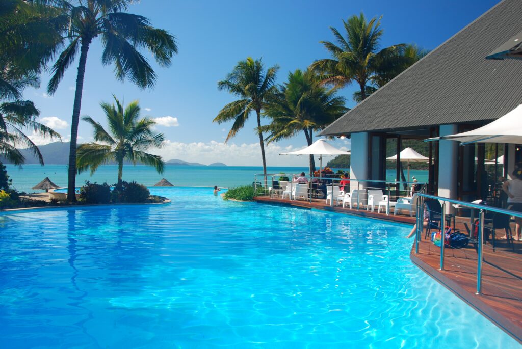 Tropical paradise wallpaper with blue skies turquoise sea lush palms and luxury pool for summer getaway