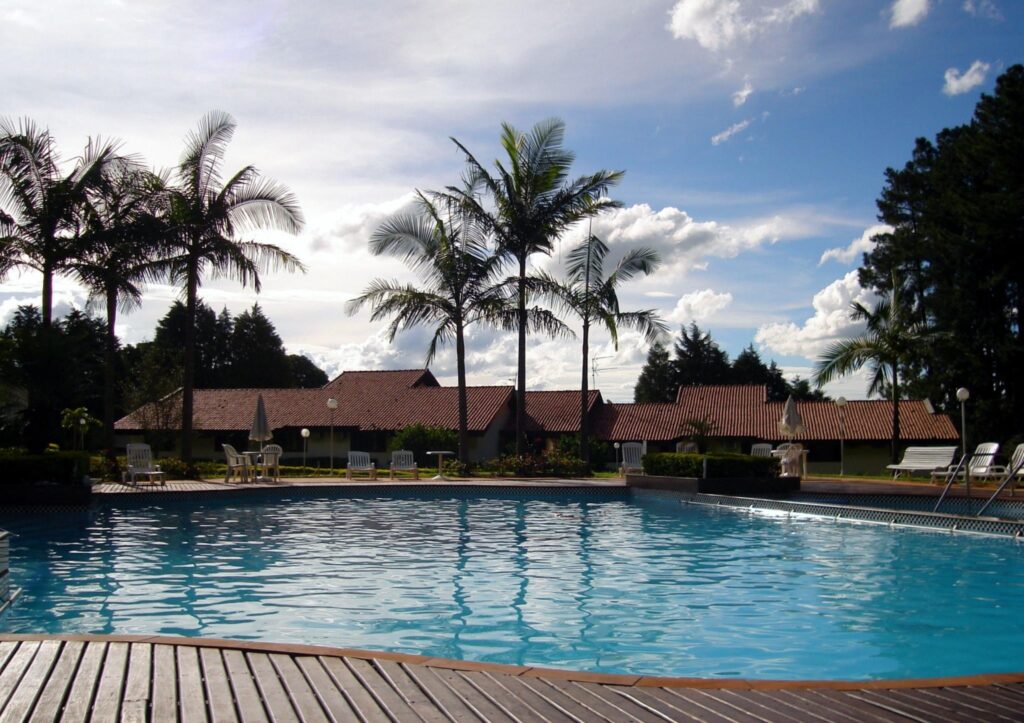 Tropical pool with cozy lodges palm trees and loungers under vibrant blue sky for relaxation Wallpaper