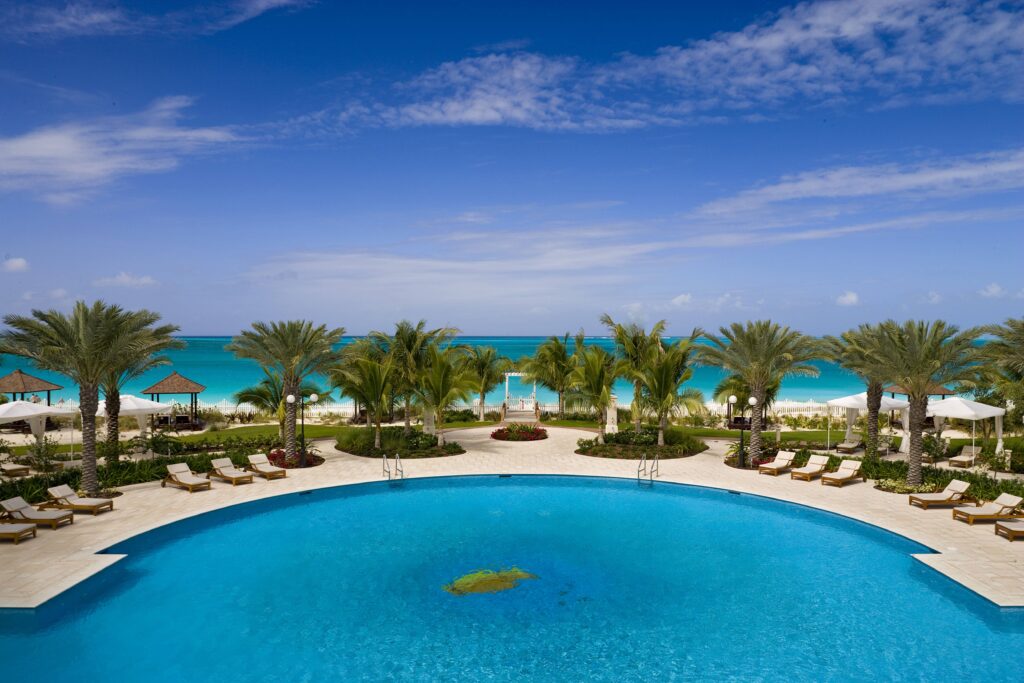 Tropical resort infinity pool with palm trees sun loungers turquoise ocean and blue summer sky Wallpaper