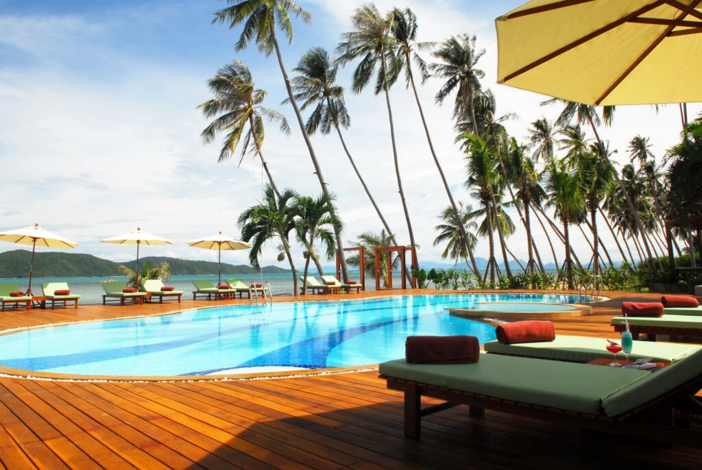 Tropical resort wallpaper with palm trees blue pool wooden loungers umbrellas ocean view greenery