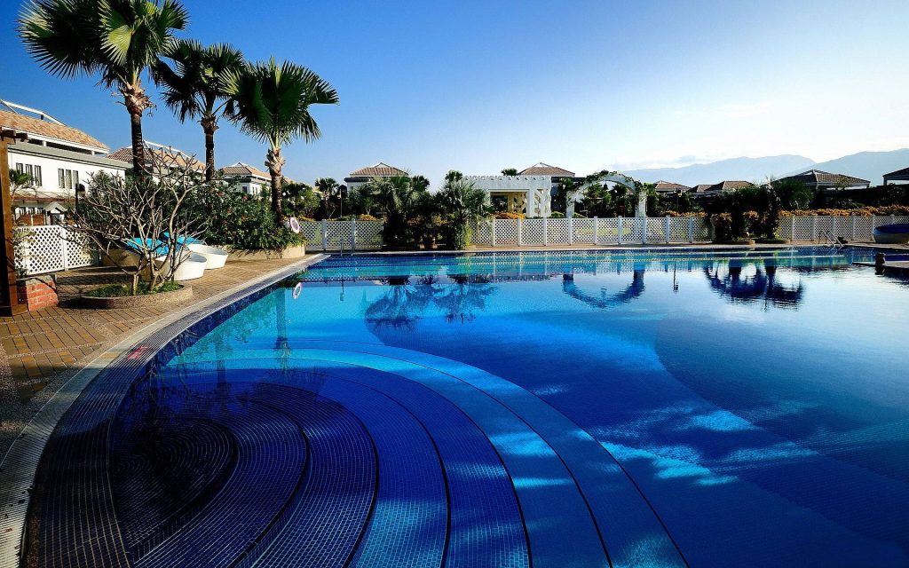 Resort pool with turquoise water palm trees and villa under clear blue sky tropical paradise wallpaper