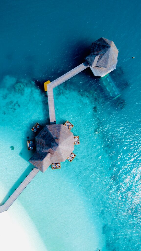 Aerial view of seaside bungalow over turquoise waters with wooden walkways and tropical beach Wallpaper