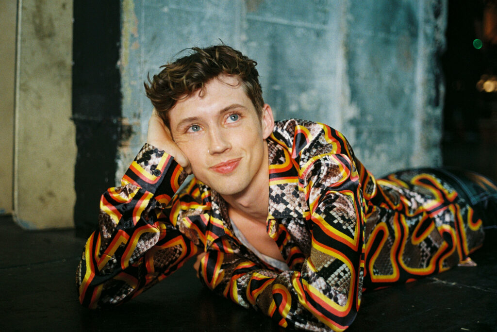 Troye Sivan relaxing backstage in vibrant patterned shirt at Pride Concert Bash wallpaper background