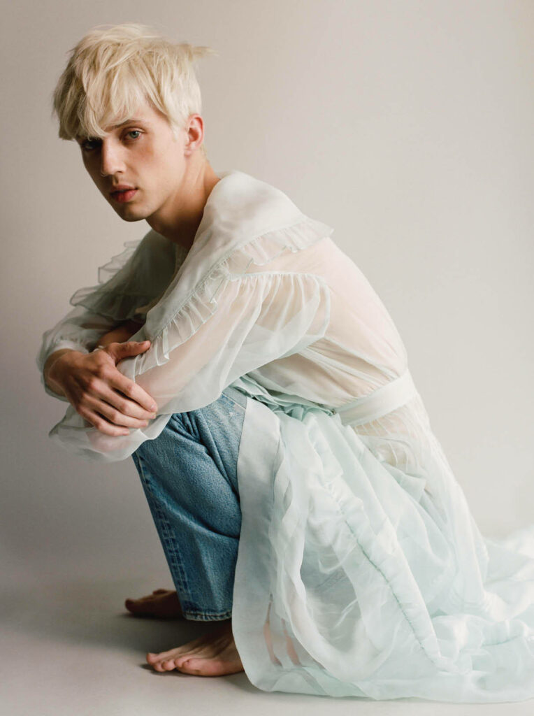 Troye Sivan barefoot in light blue jeans and sheer white ruffled top soft natural light wallpaper