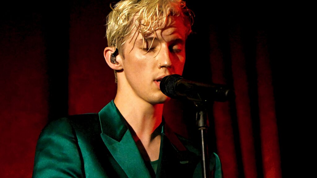 Troye Sivan singing live on stage with microphone red backdrop signature style charisma Wallpaper