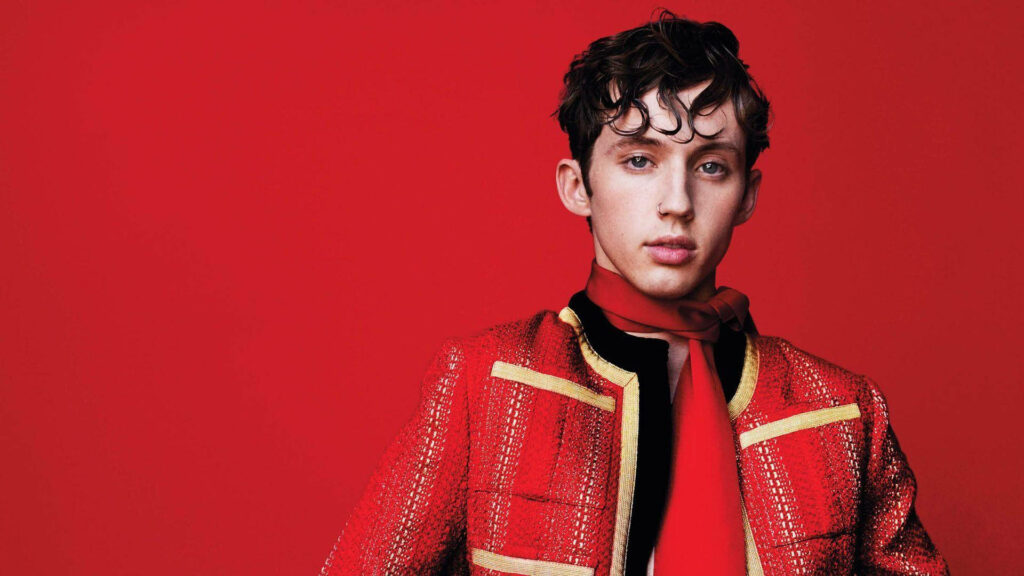 Troye Sivan in stylish red outfit posing confidently against bold red background for V magazine Wallpaper