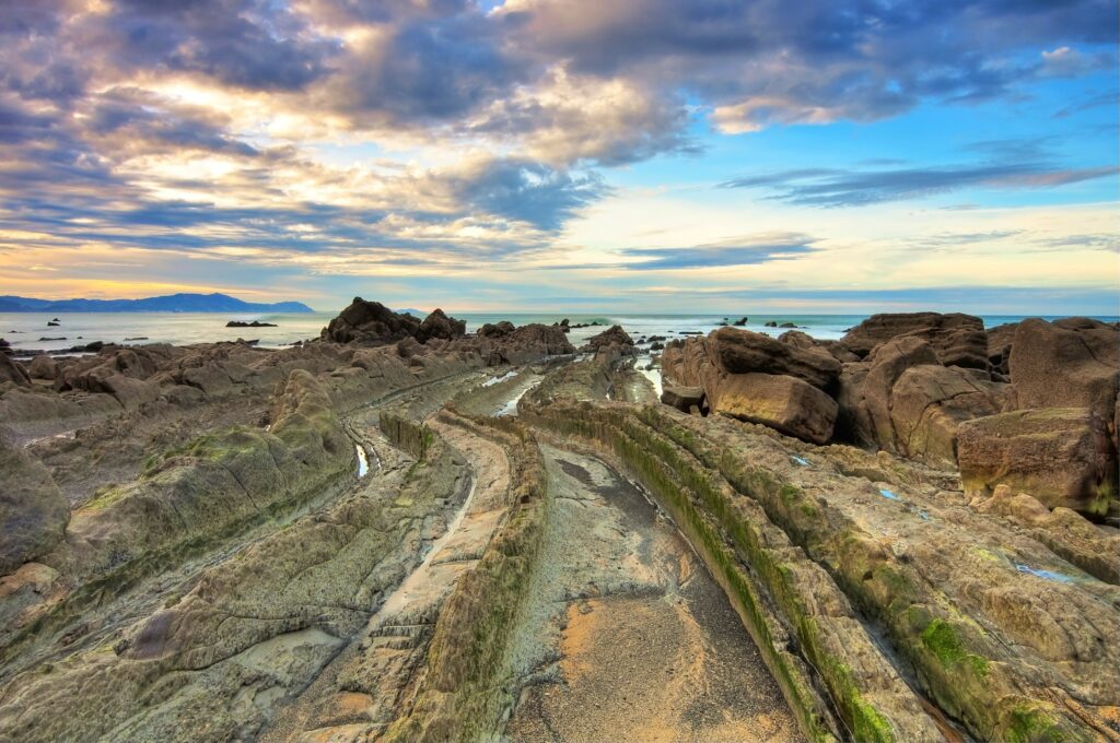 Turbidite rock formations along Spanish coast with layered rocks moss and vivid blue sky wallpaper