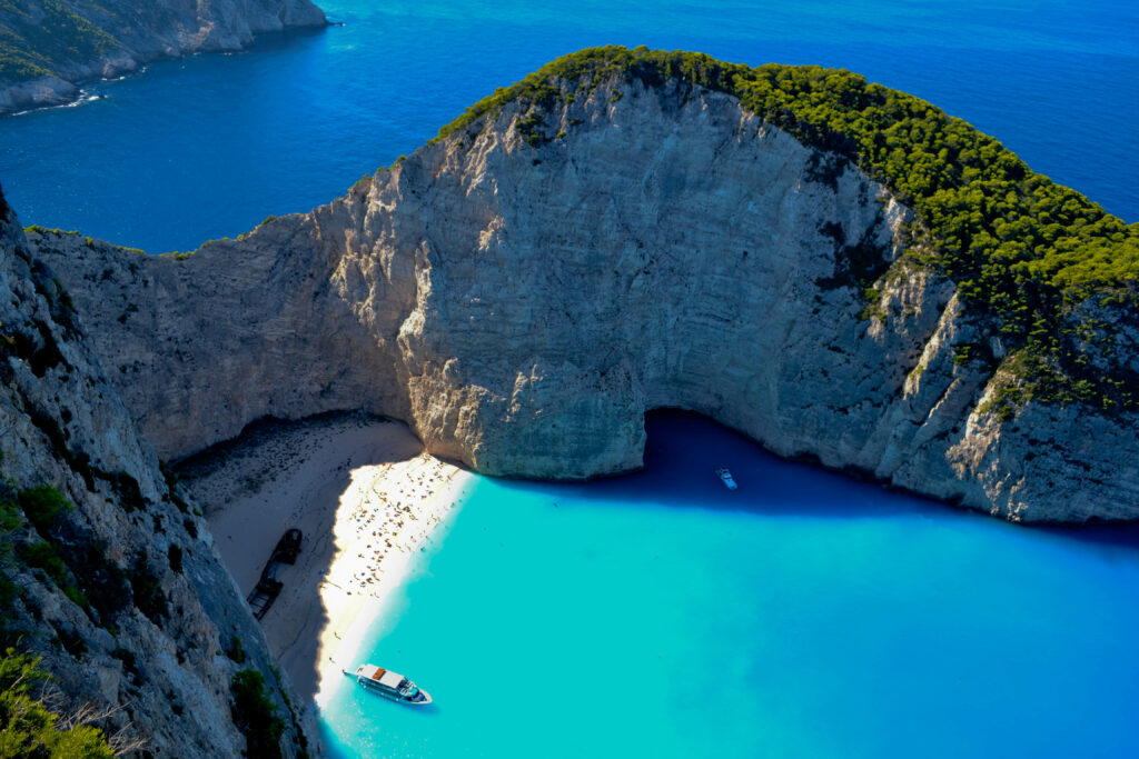 Aerial view of turquoise bay with boats near white sand beach and lush rocky cliffs wallpaper