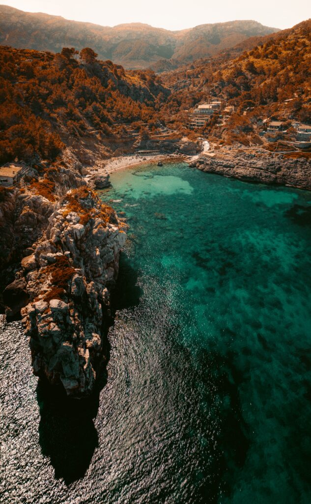 Aerial view of turquoise bay with rugged rocks golden coast and lush hills in warm sunlight Wallpaper