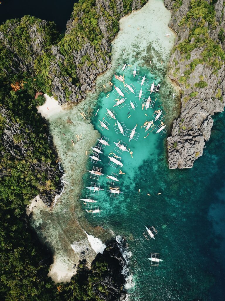 Aerial view of turquoise bay with traditional boats cliffs and green tropical shoreline wallpaper
