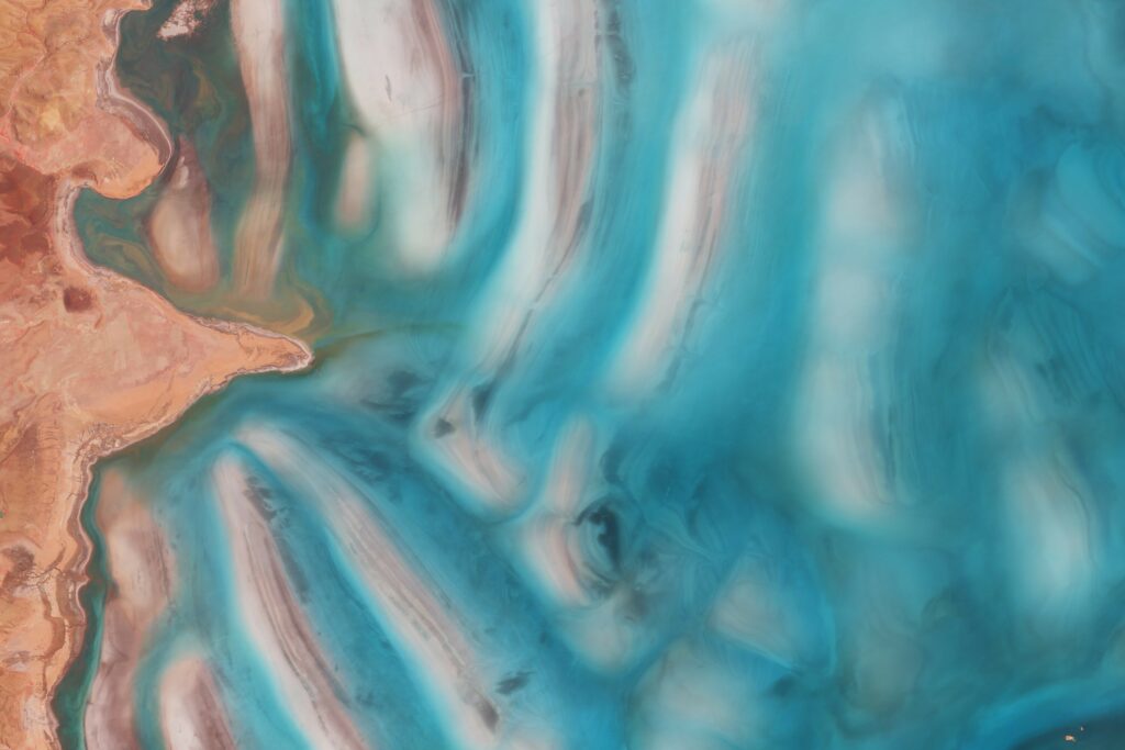 Aerial view of coastal landscape with turquoise water swirling against textured sand and earth Wallpaper