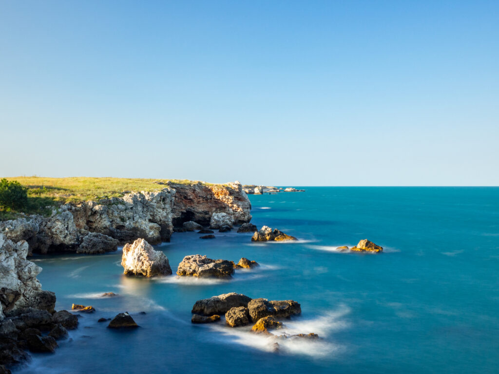 Serene coastal landscape with rugged rocks and turquoise sea under clear blue sky wallpaper