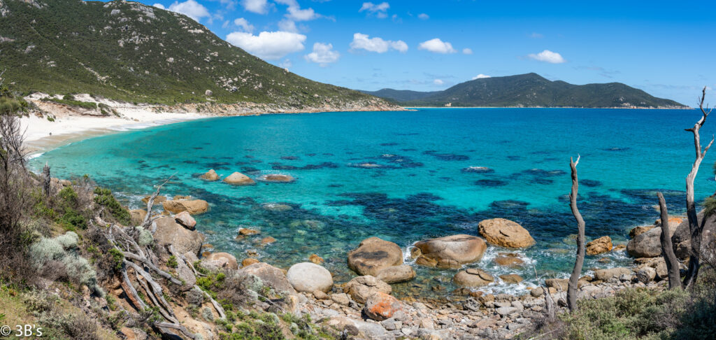 Vibrant coastal landscape with turquoise sea rugged rocks and green mountains under blue sky wallpaper