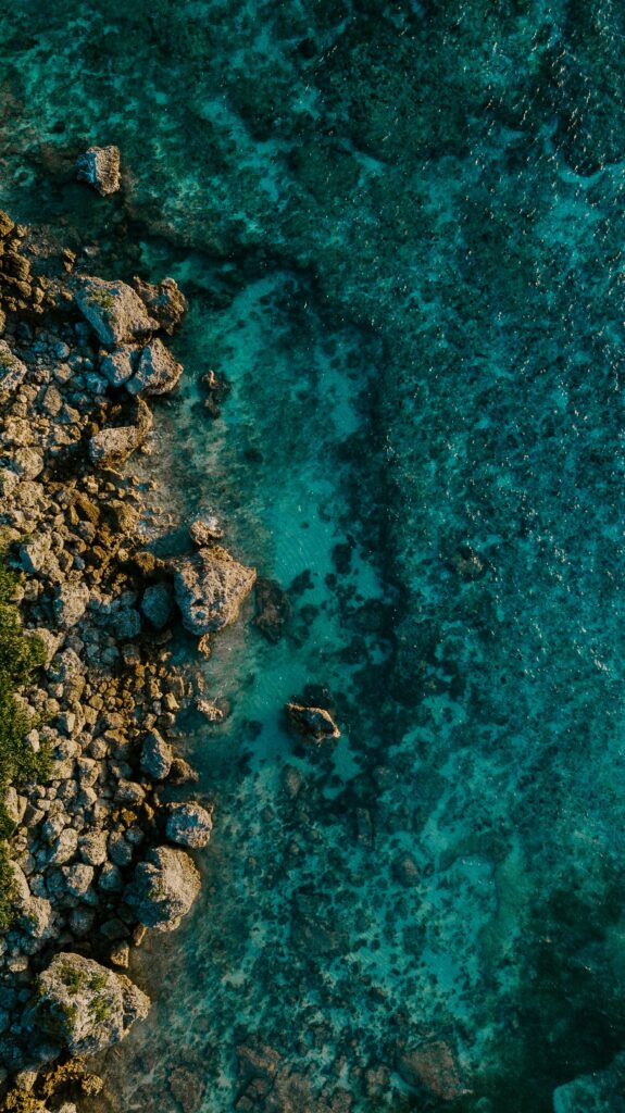 Aerial view of rocky shoreline with clear turquoise water and weathered stones coastal wallpaper