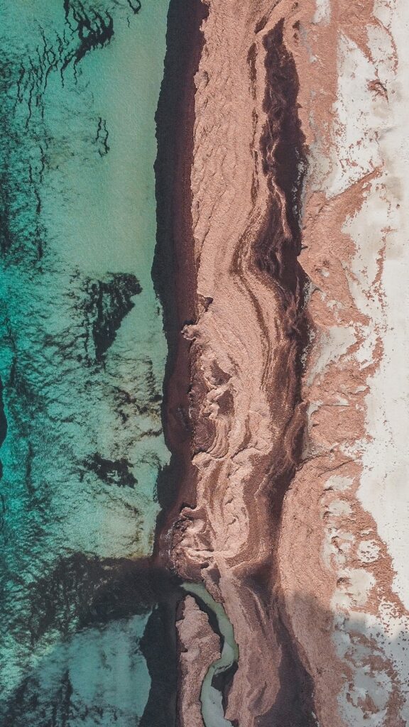Aerial view of turquoise sea meeting sandy beach with unique coastal textures and landforms Wallpaper