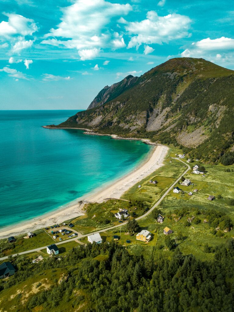 Aerial view of turquoise sea meeting golden beach with green fields and mountains backdrop wallpaper