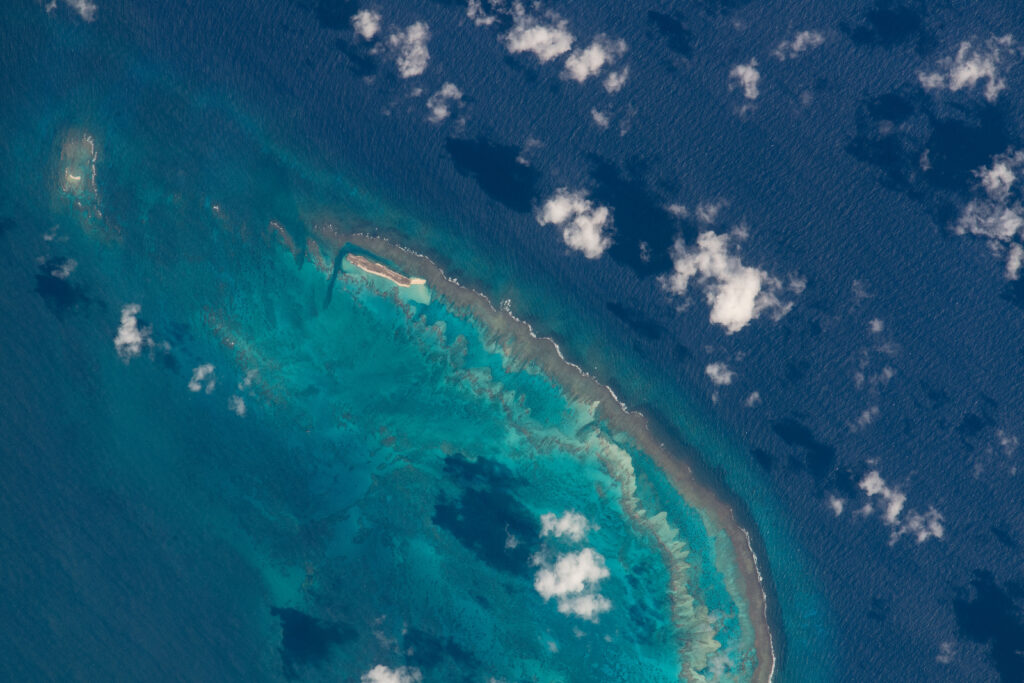 Aerial view of vibrant turquoise coastline with coral patterns white clouds and deep blue sea Wallpaper