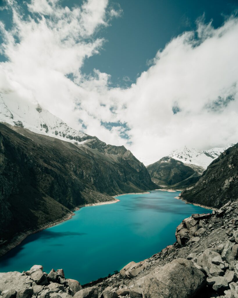Turquoise lake surrounded by rugged snow-dusted mountains and dynamic cloudy sky wallpaper background