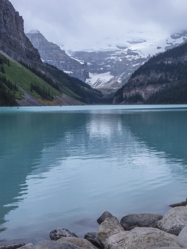Turquoise lake with rugged stone shores and green mountains beneath snow-capped peaks landscape Wallpaper