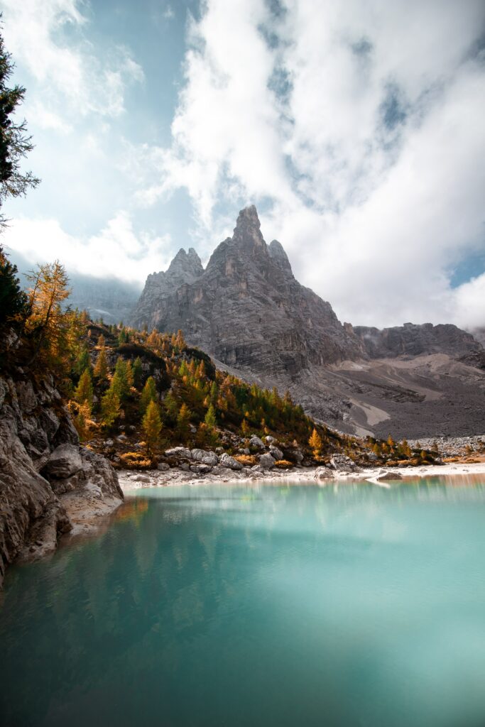 Turquoise lake reflecting towering mountain peaks framed by rocky shores and autumn trees Wallpaper