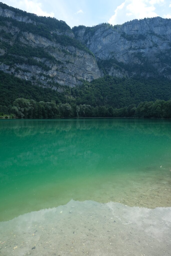 Turquoise lake reflecting green forest and rocky cliffs under bright sky serene nature wallpaper