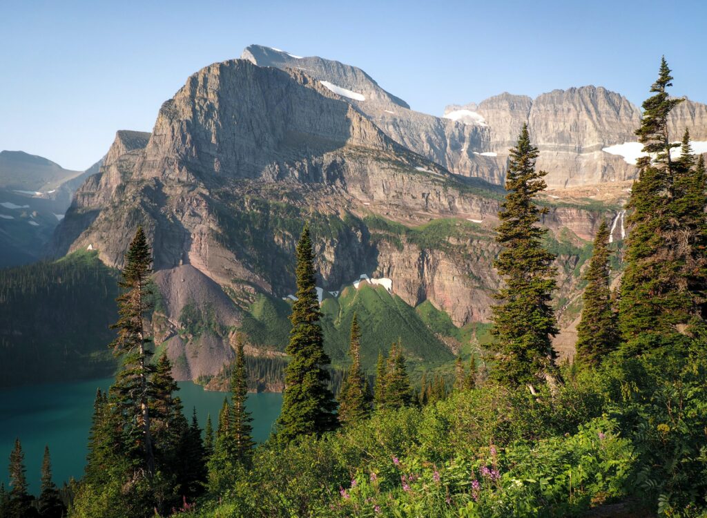 Rugged mountains reflected in turquoise lake framed by spruce trees under clear blue sky wallpaper