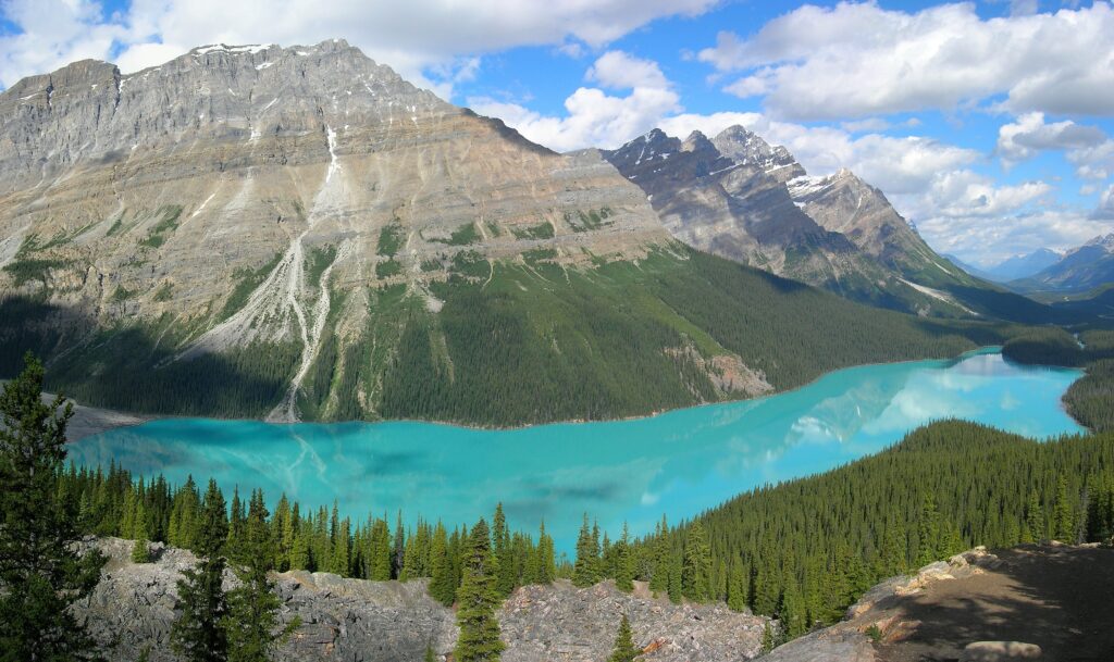 Turquoise lake surrounded by rugged mountains and lush conifer forests reflecting clear sky wallpaper