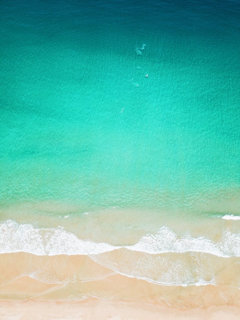 Aerial view of tranquil beach with turquoise waves gently rolling onto soft sandy shore wallpaper