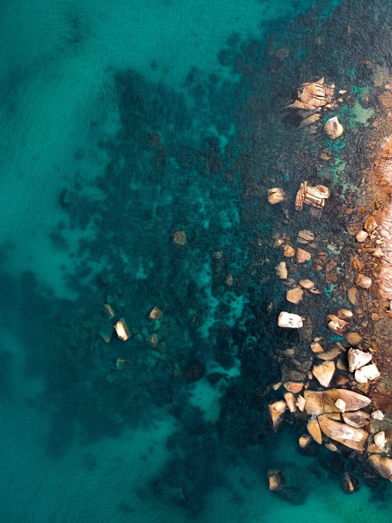 Aerial view of clear turquoise ocean with visible rocks and natural ripples coastal wallpaper