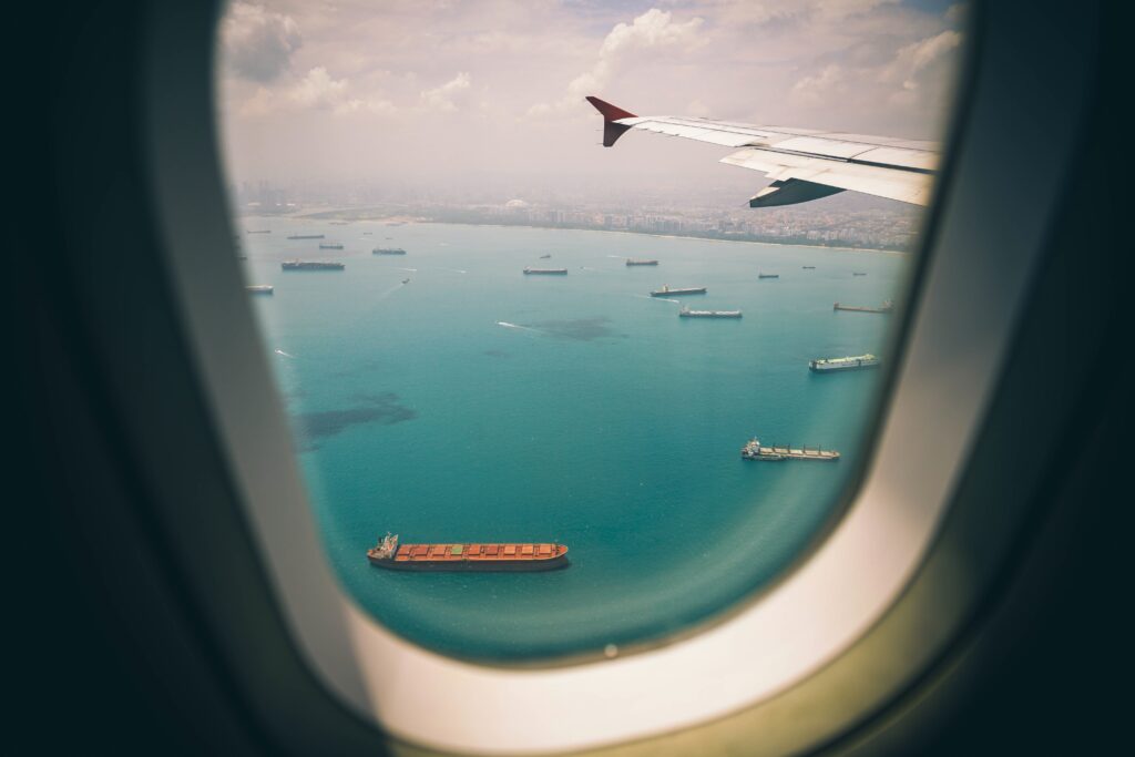 Top view of turquoise sea with ships and airplane wing seen through porthole wallpaper background