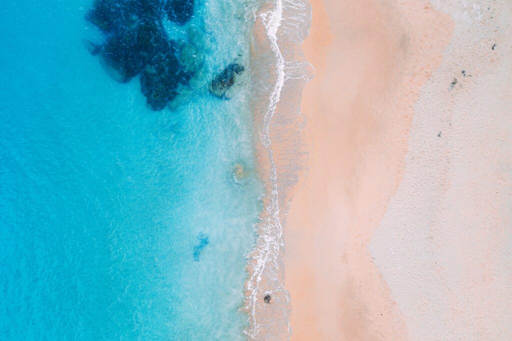 Aerial view of turquoise ocean waves gently washing over smooth pale sandy beach wallpaper background